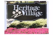Heritage Village at Lawrence sign with landscaping and pink flowers in front.