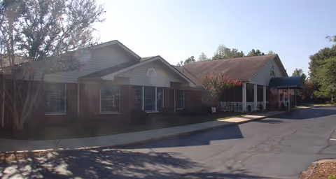 Exterior view of a single-story brick and siding building with a covered entrance and an American flag, surrounded by trees and a paved driveway under a clear sky.