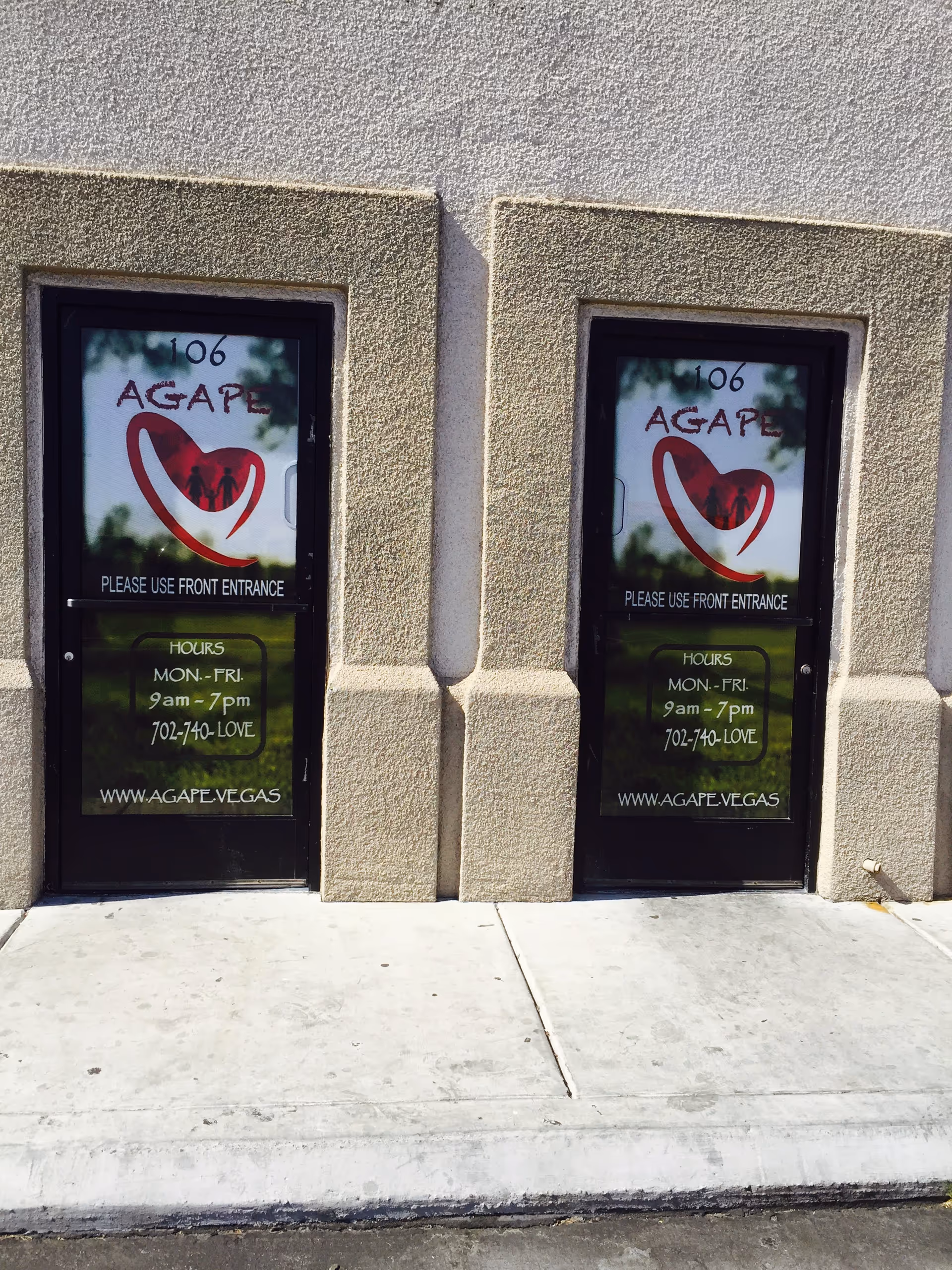 Two glass doors showing AGAPE signage and front entrance hours for the facility.