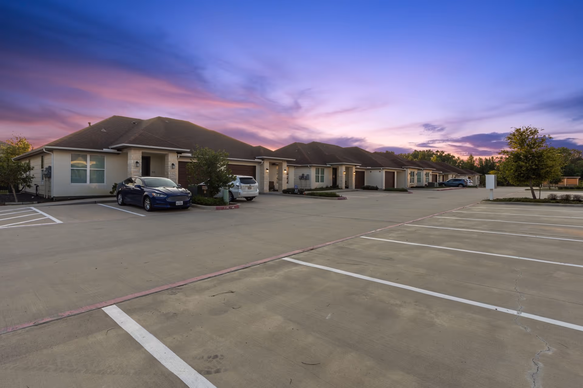 Row of single-story senior living cottages along a parking lot at dusk