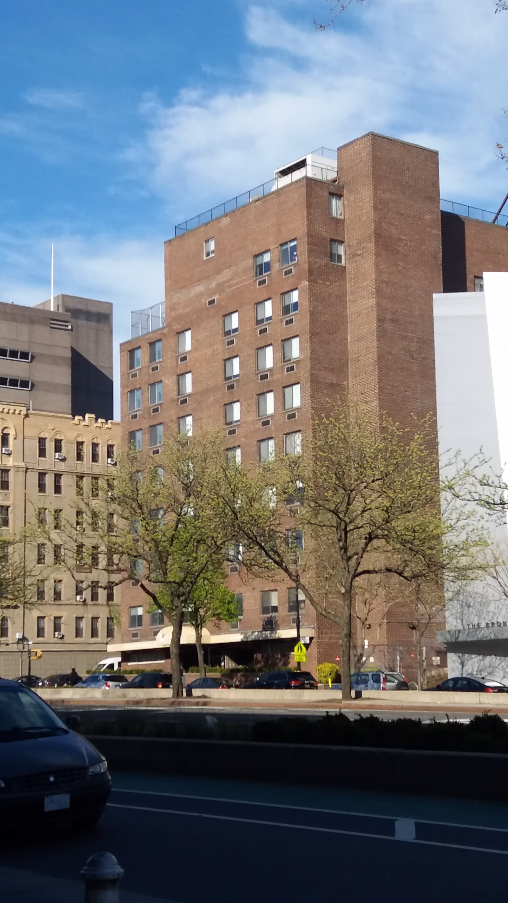 Tall brick building along a city street with trees and parked cars.