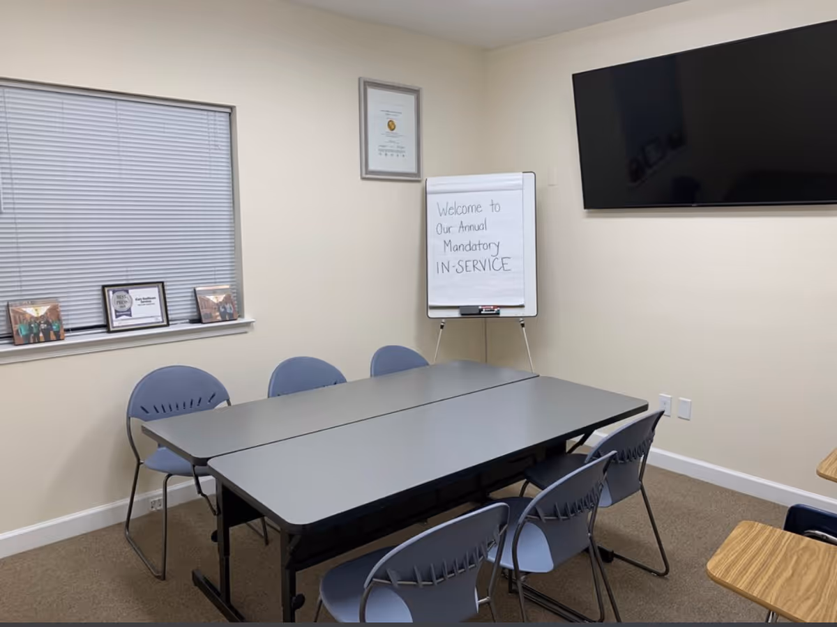 A conference room with folding tables, blue chairs, a whiteboard, and a large wall-mounted TV.