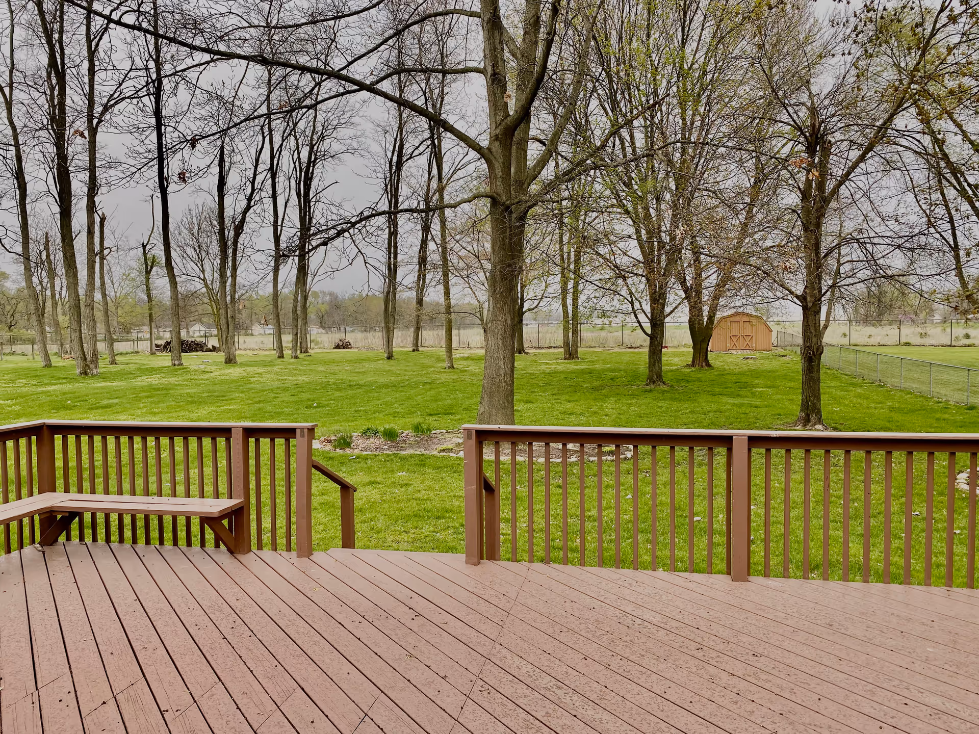 Wooden deck overlooks a green lawn with trees and a small shed in the distance.