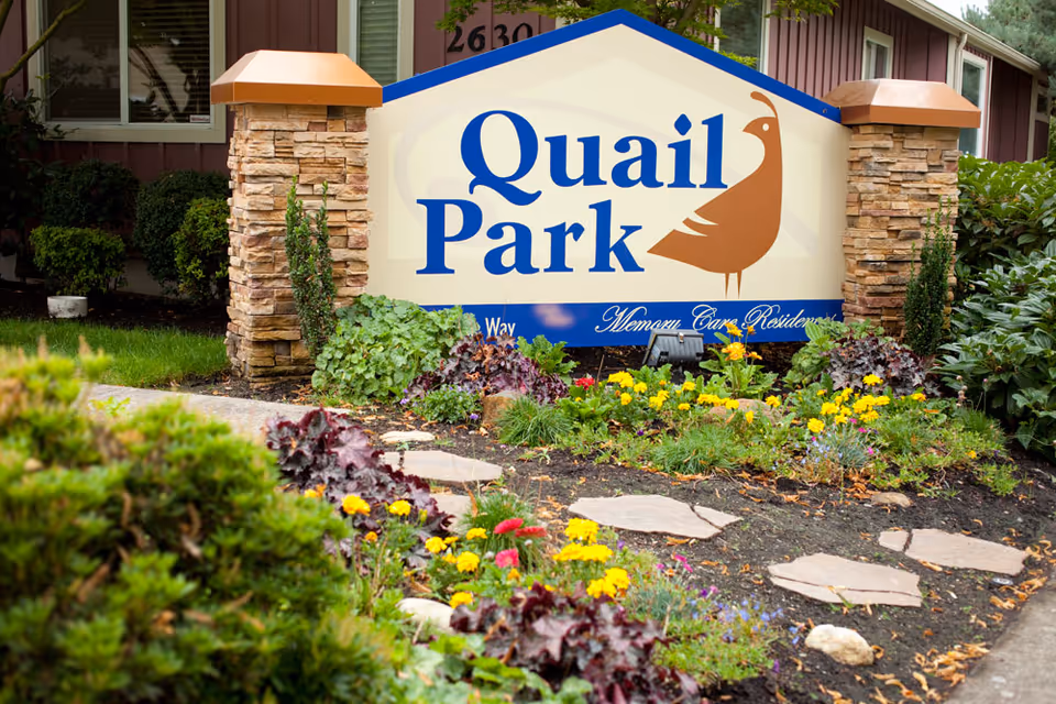 Landscaped entrance sign reading 'Quail Park' with stone pillars and colorful flowers in front.