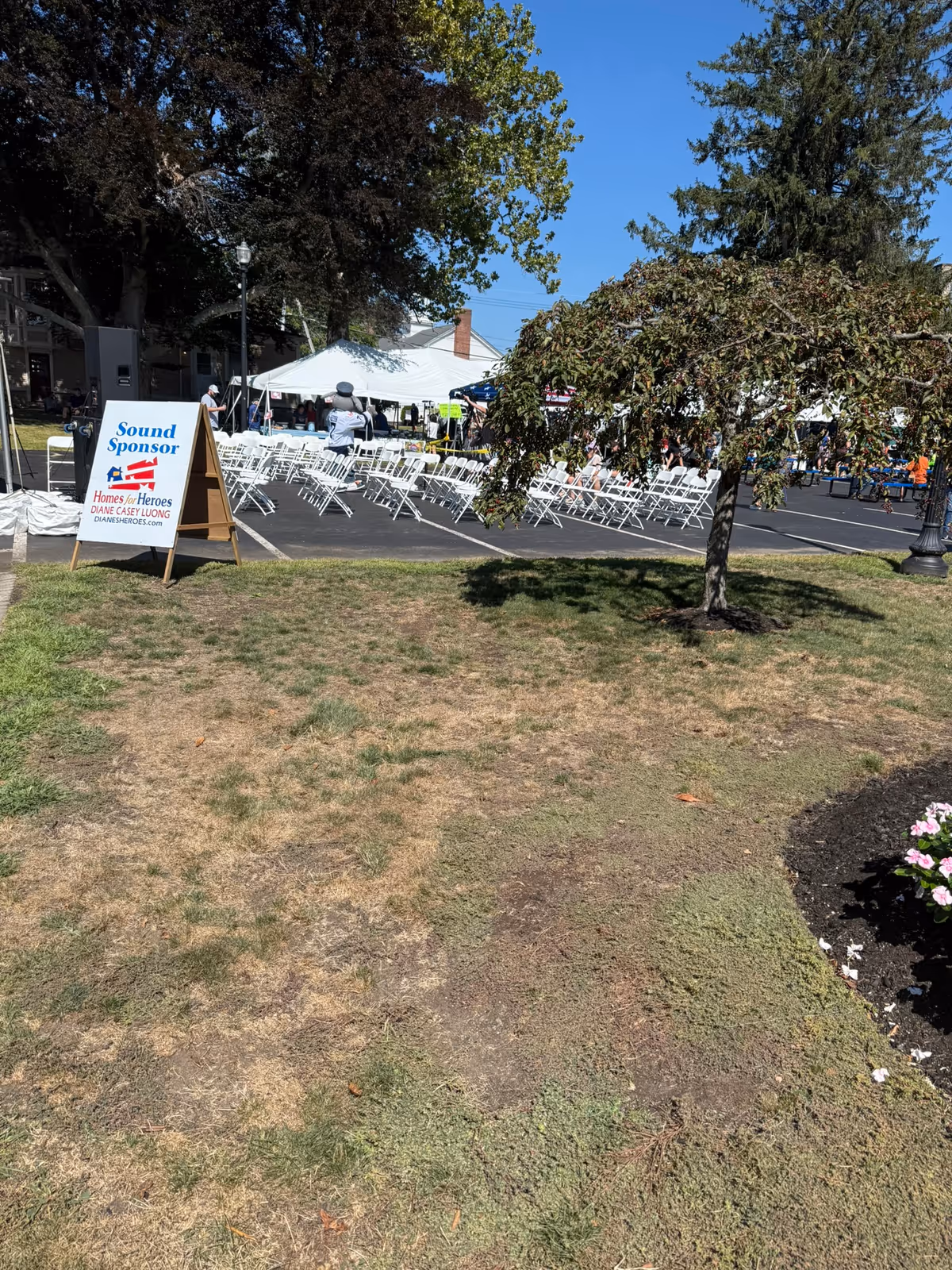 Outdoor event with white chairs set up under tents and trees