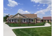 Single story brick senior living building with curved walkway and manicured lawn under blue sky.