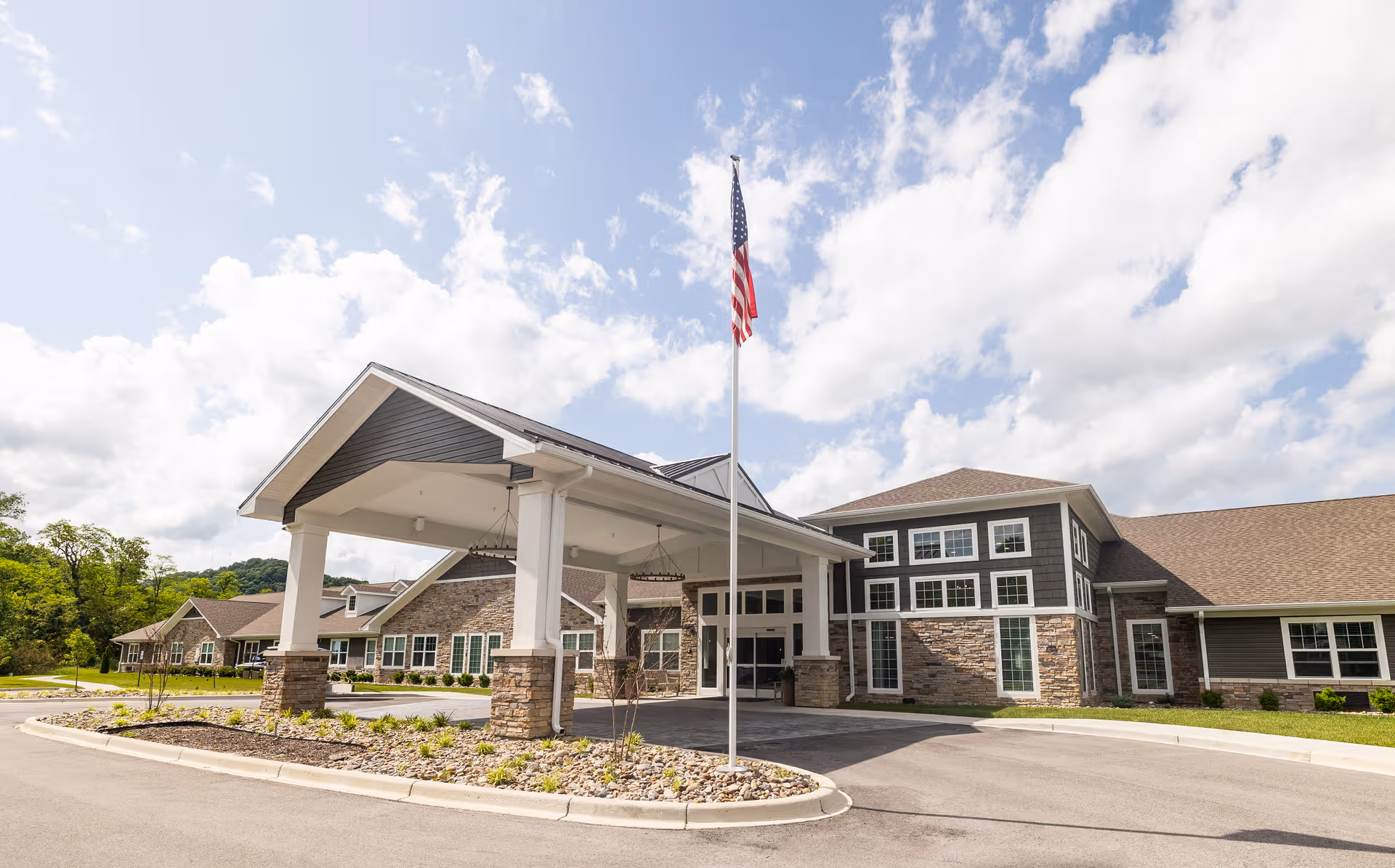 Exterior view of Rivercrest Senior Living with a covered entrance, flagpole, and landscaped surroundings.