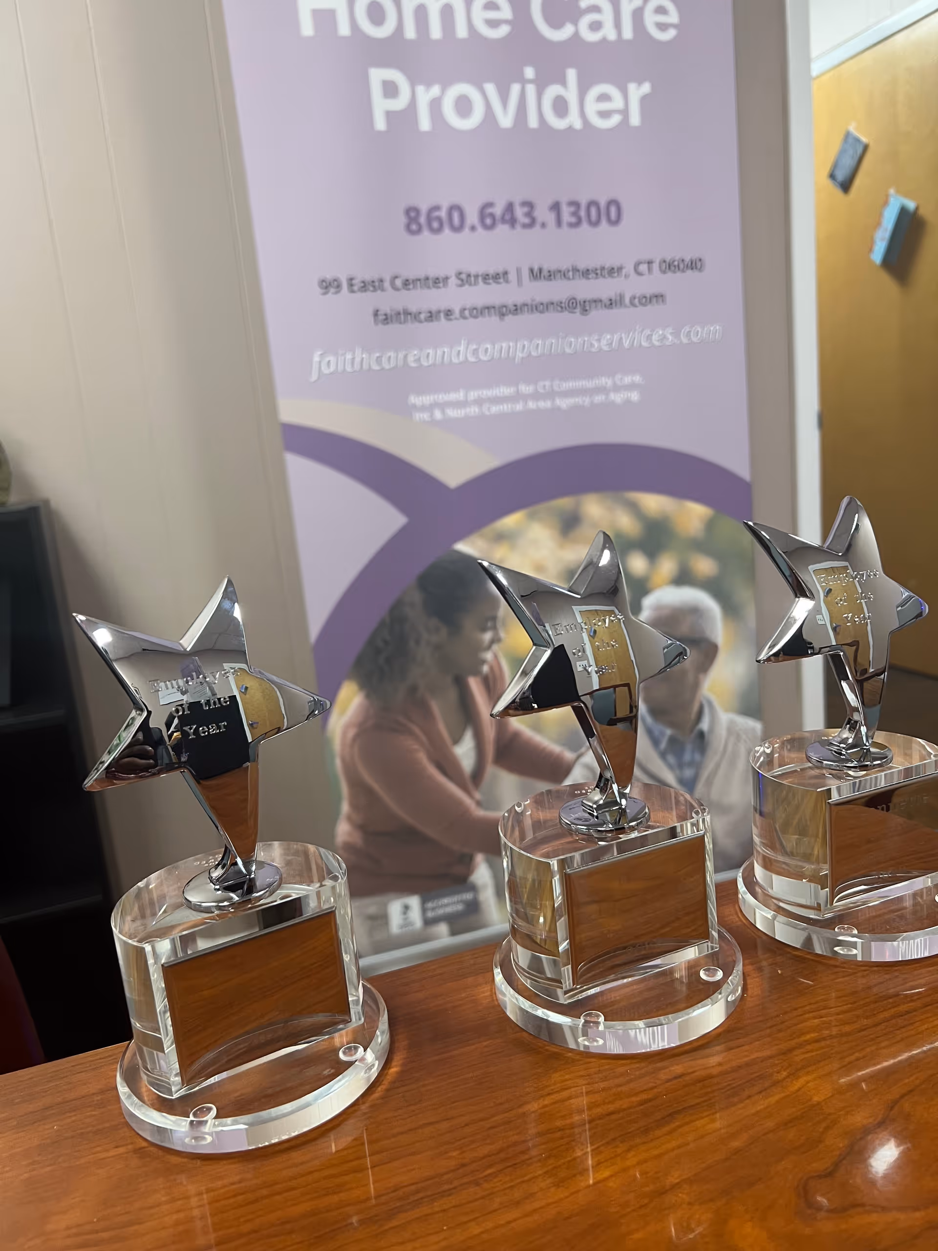Trophies with star-shaped tops sit on a wooden table, with a purple banner in the background.