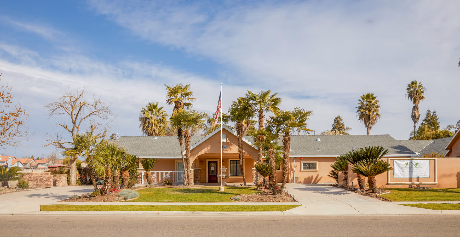 Front view of a single-story senior living facility with palm trees and flagpole.