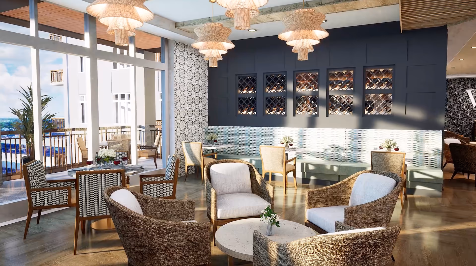 Sunlit communal dining and lounge area with wicker and upholstered chairs, round tables, pendant lights, and large windows overlooking a balcony.