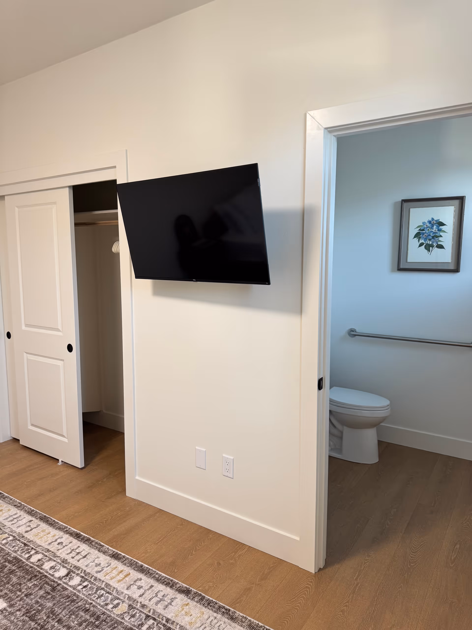 Wall-mounted TV on a wall between a closet and a bathroom in a suite.