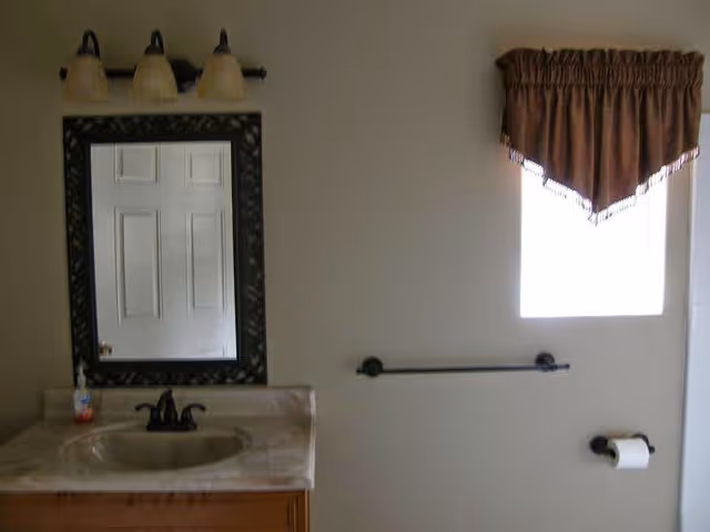 Bathroom featuring sink, mirror, three-light fixture, window with valance, and towel bar.
