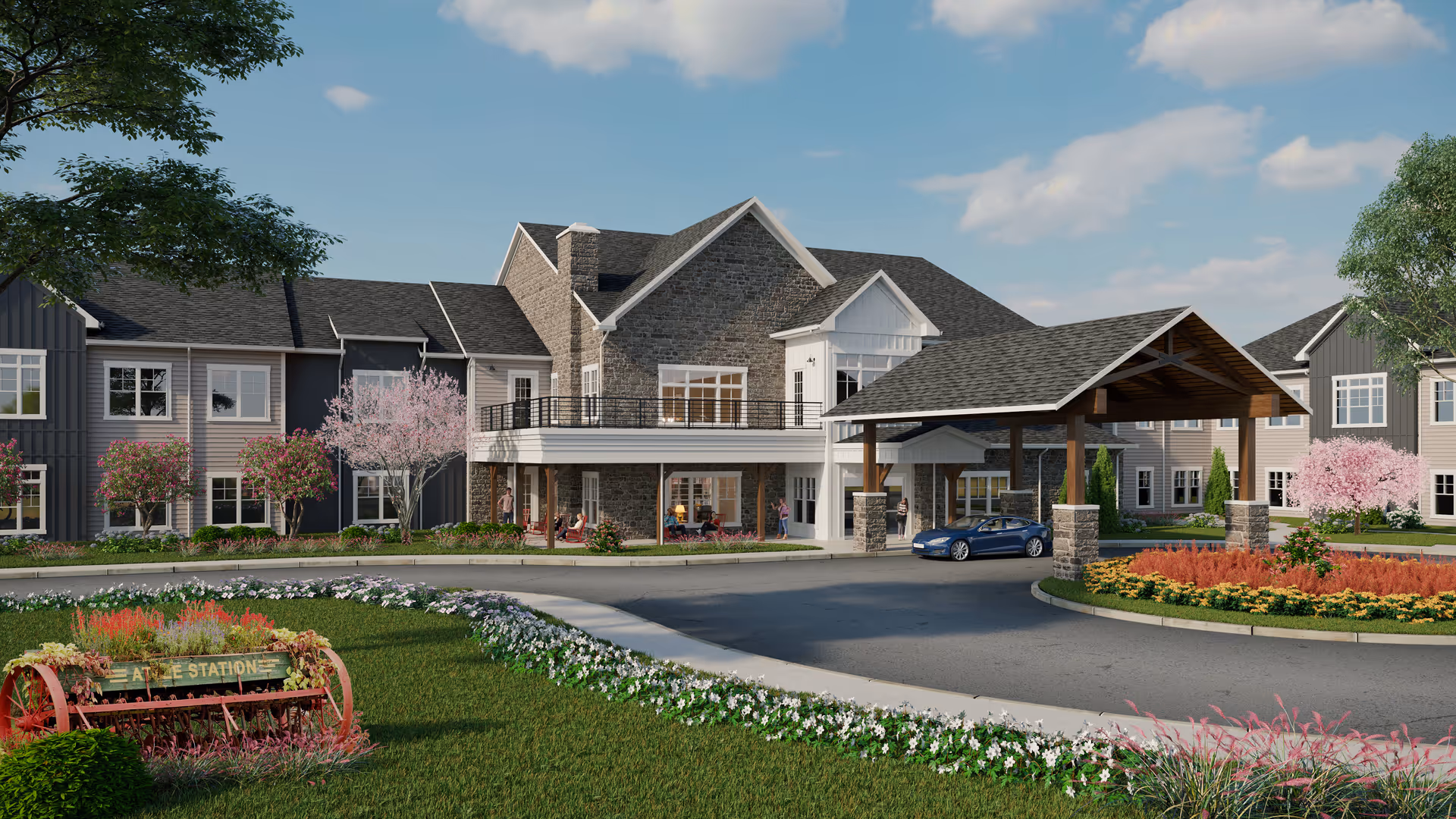 Exterior view of a senior living facility with a large covered entrance driveway, landscaped gardens with flowers and trees, and a multi-story building featuring stone and siding exterior under a partly cloudy sky.