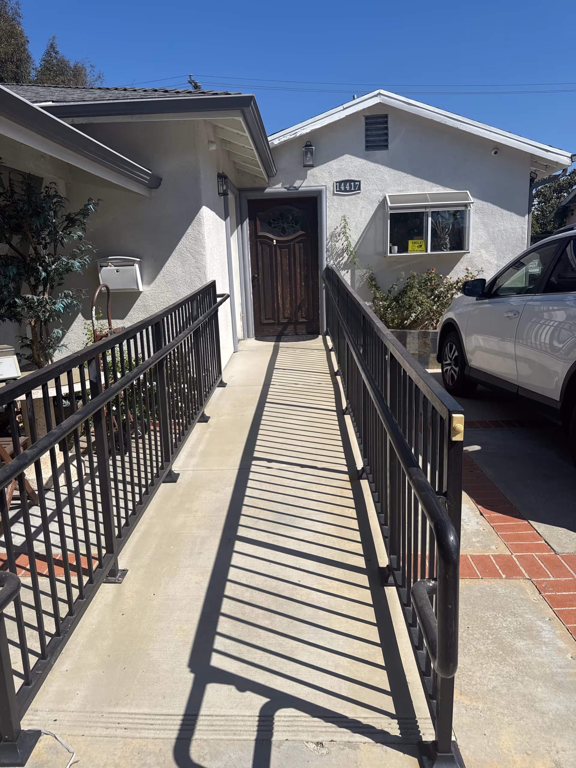 Ramp with metal handrails leads to a front door of a building beside a parked car.