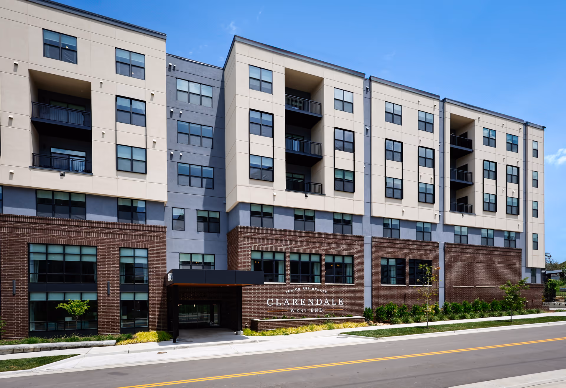 Modern multi-story senior living building with brick base and light facade, signage reading Clarendale West End.