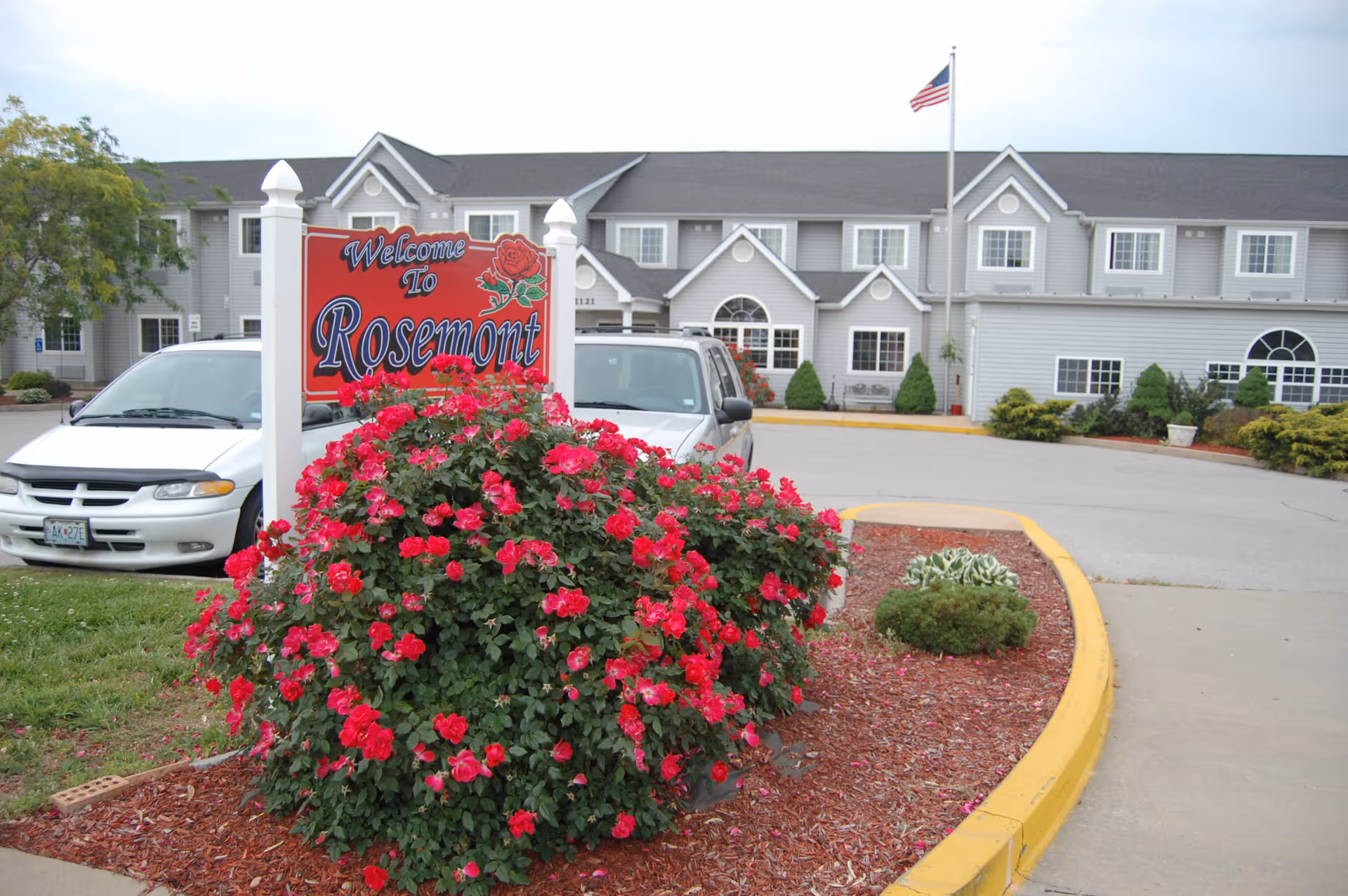 Exterior view of Rosemont Senior Living Centre with a red rose sign and parked cars.