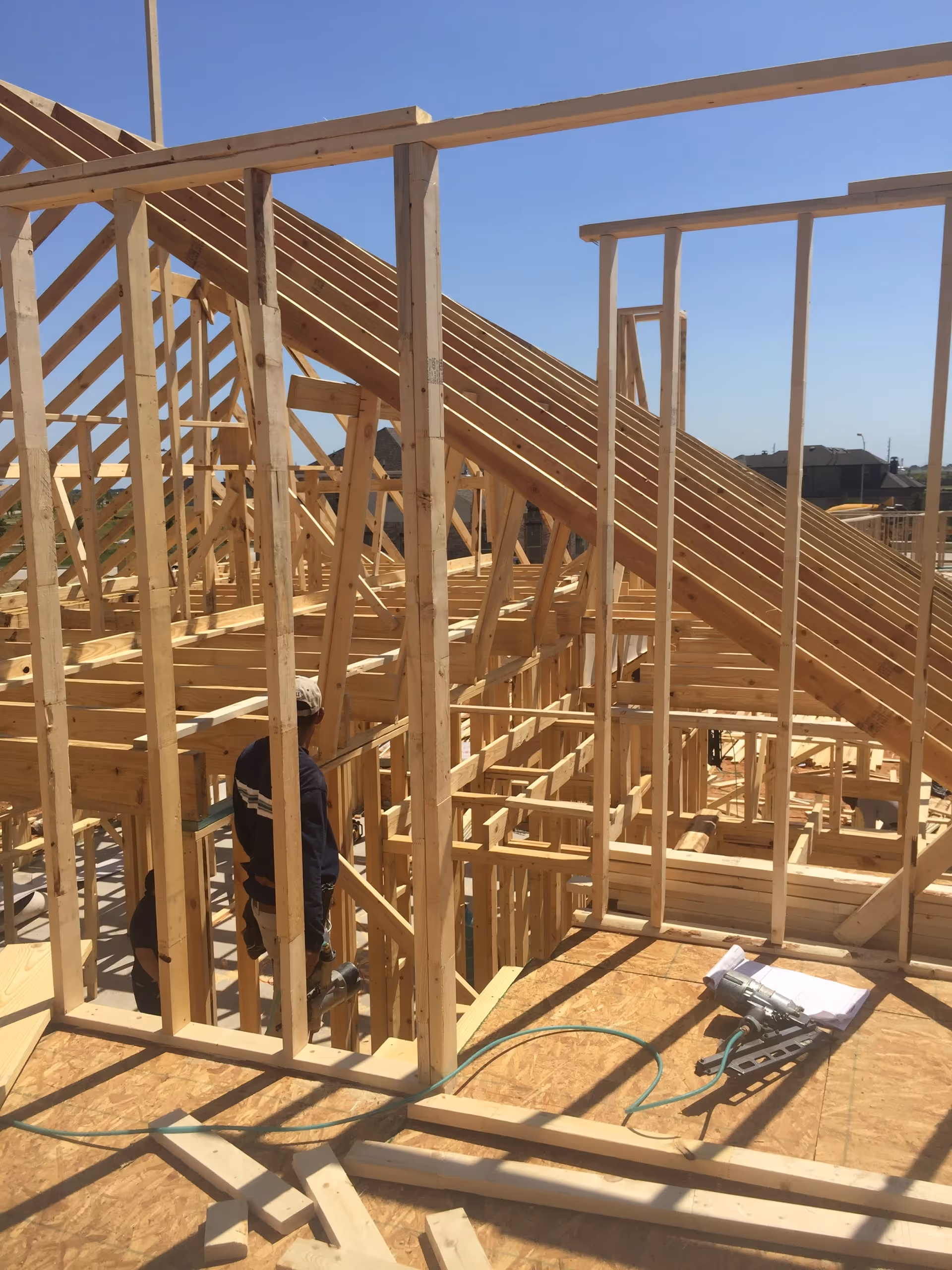 Unfinished wooden house framing under construction with a worker on site.