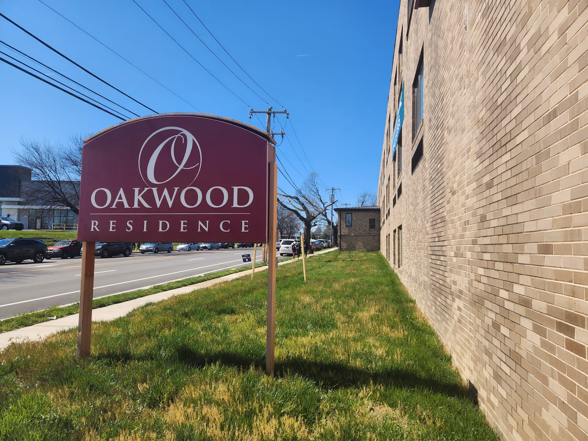 Front view of Oakwood Residence sign beside a brick building and street.