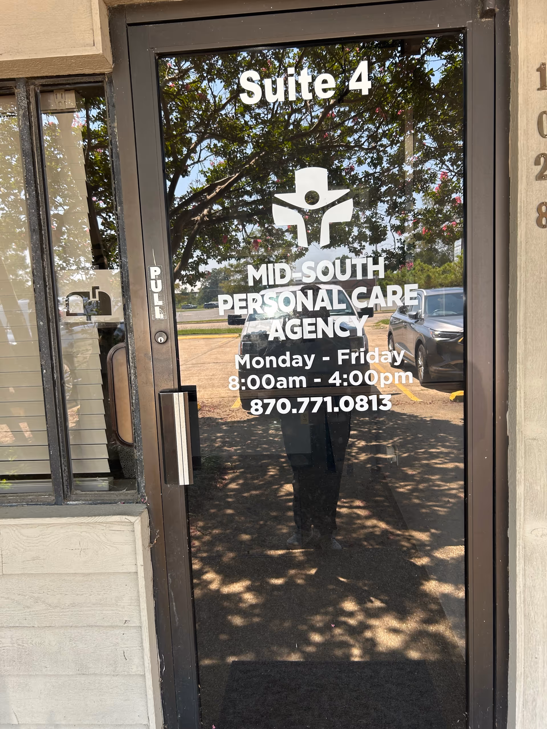 Glass door shows Suite 4 and Mid-South Personal Care Agency signage, reflecting trees and cars.