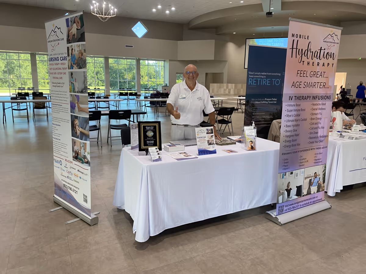 Man stands behind a brochure-filled table at an indoor expo booth for Morgan Star Home Care.