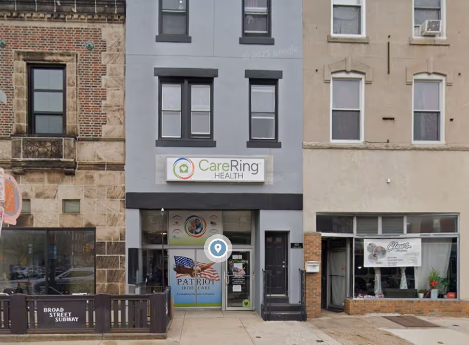 Street-level view of Patriot Home Care storefront between brick and gray buildings.