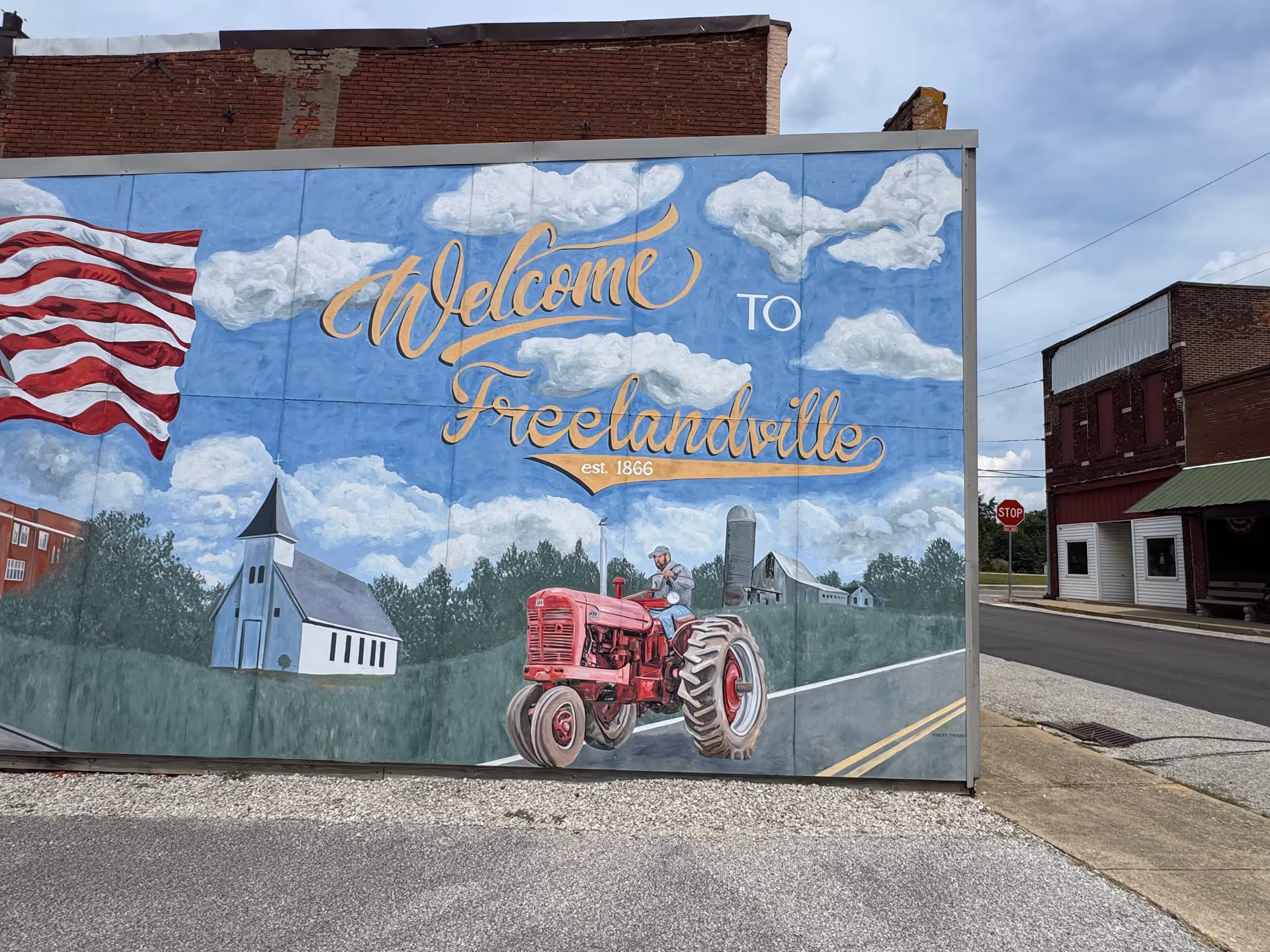 A mural on a brick building reads Welcome to Freelandville with a tractor scene.