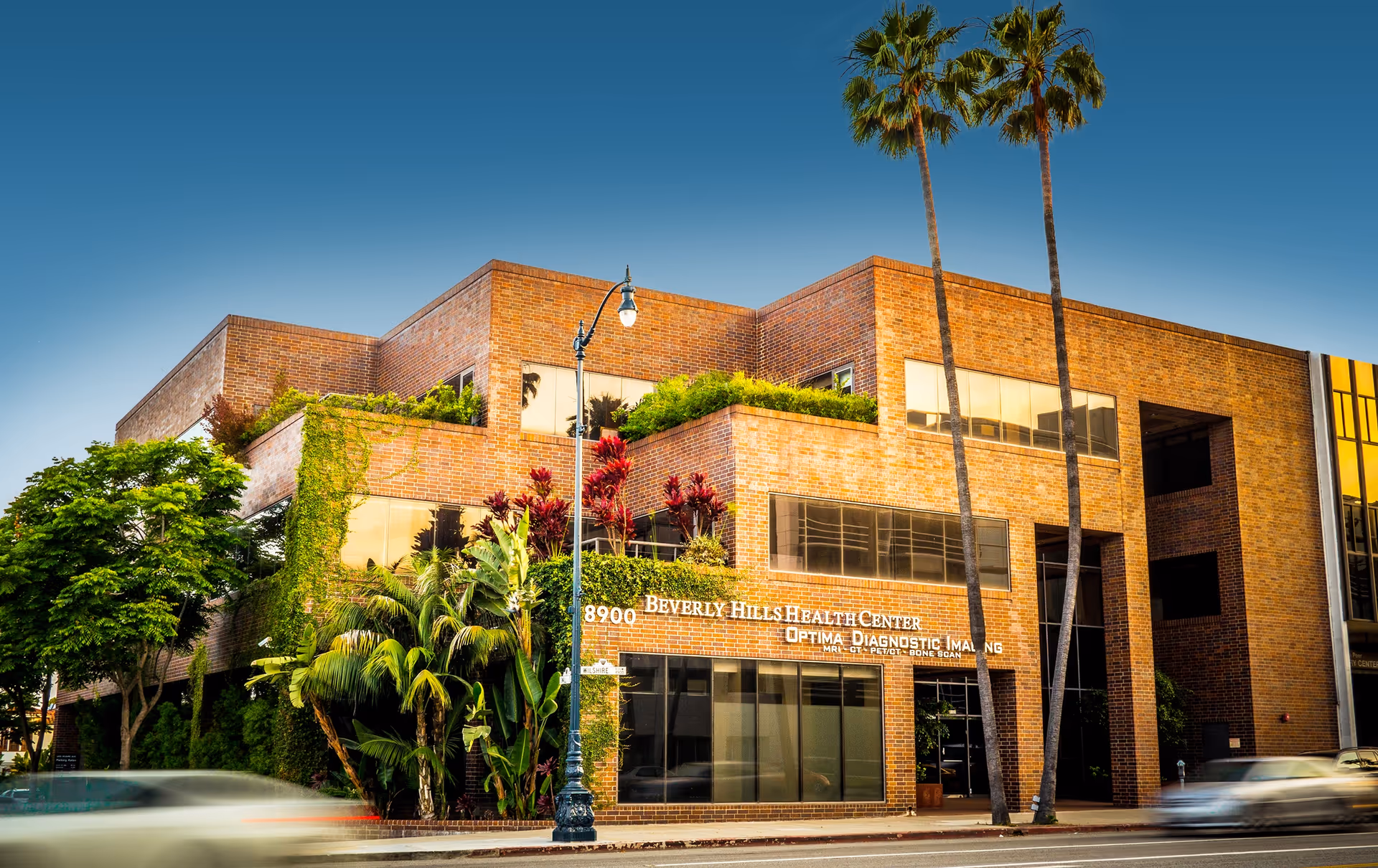 Brick building front with Beverly Hills Health Center sign, greenery, and palm trees.