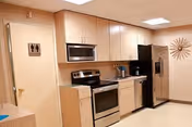 Senior living facility kitchenette with cabinets, stove, microwave, and refrigerator along beige walls.