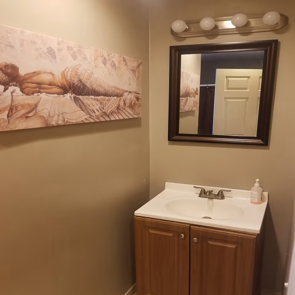 Small bathroom with sink, mirror, cabinet, wall art, and soap dispenser.