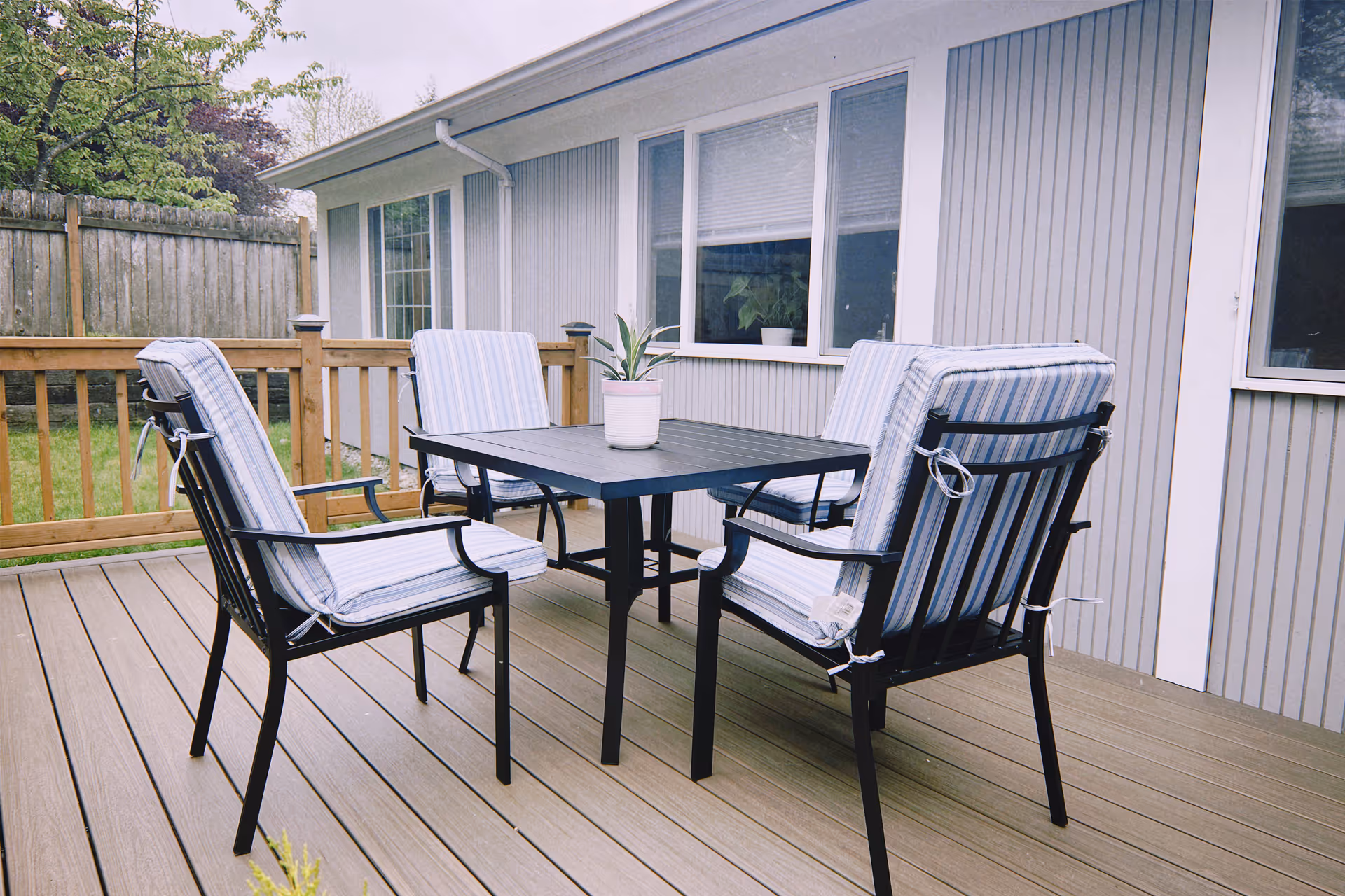 Outdoor deck with a table and cushioned chairs beside a gray home.