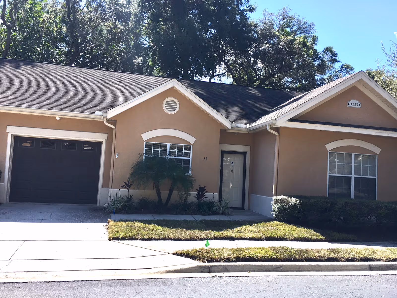 Beige, single-story senior living building with a garage door, main entrance, and manicured shrubs.