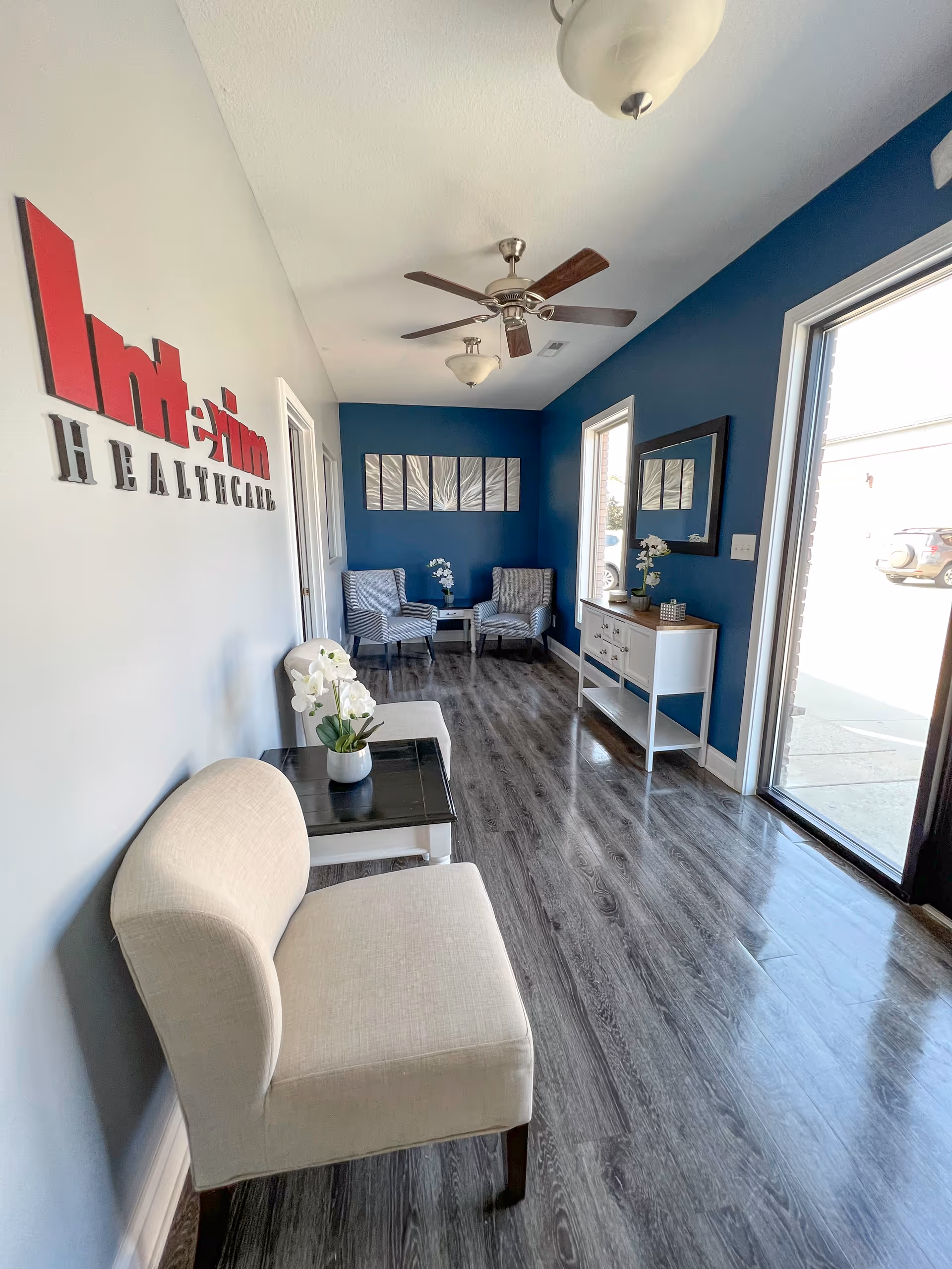 Reception lobby with blue walls, ceiling fans, modern seating, and Interim HealthCare sign.