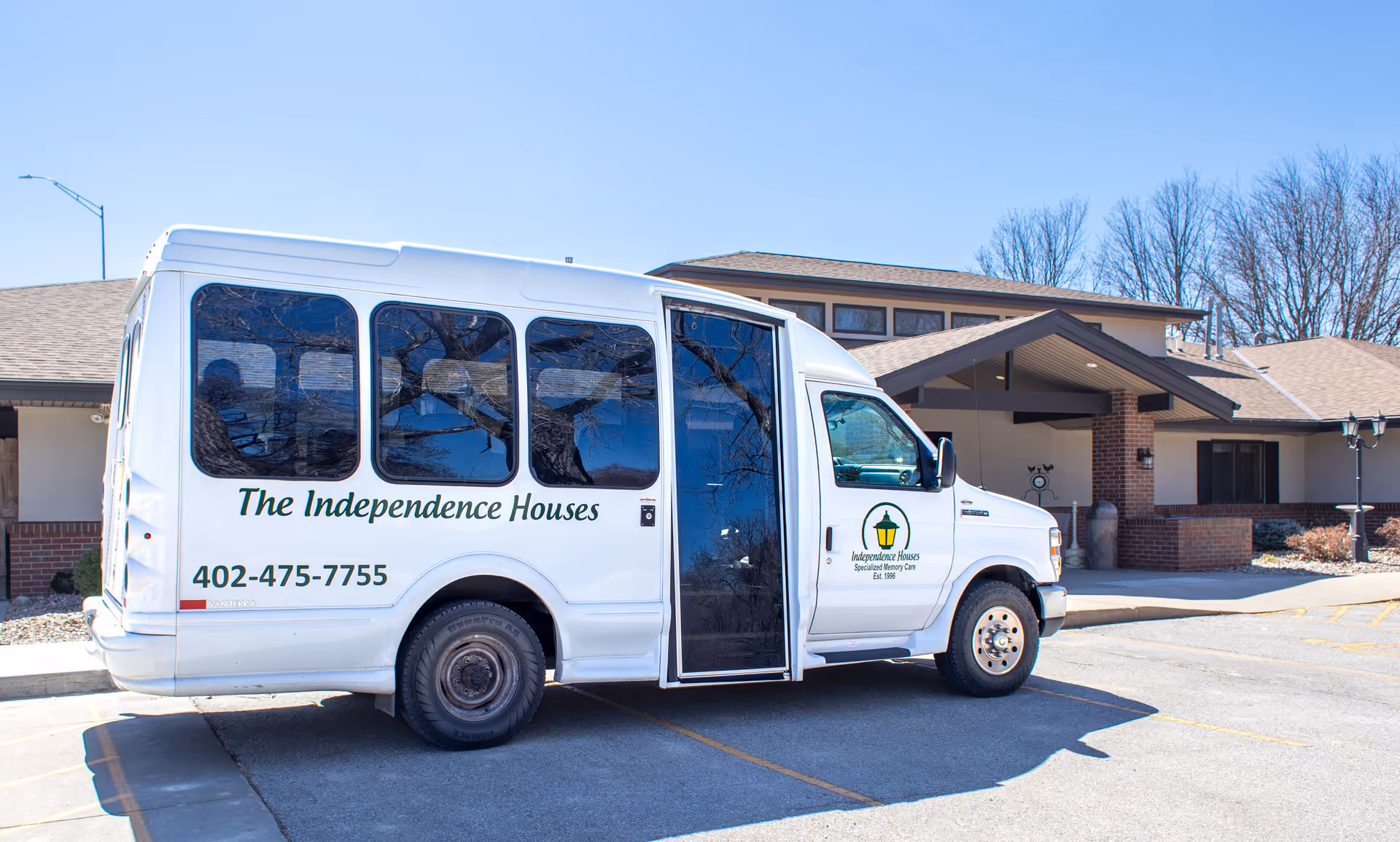 White van labeled The Independence Houses parked in front of a beige senior living facility.