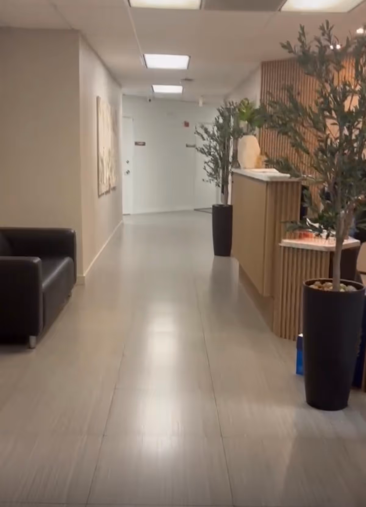 Long, well-lit hallway in a senior care facility with plants and a reception desk.