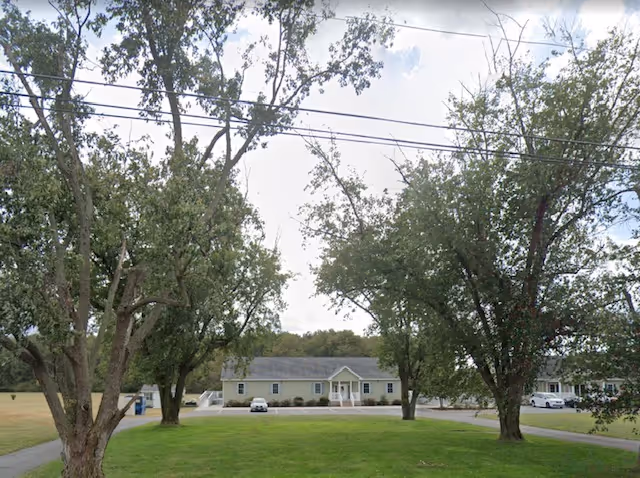 Delmar Manor assisted living building front view with trees and lawn.