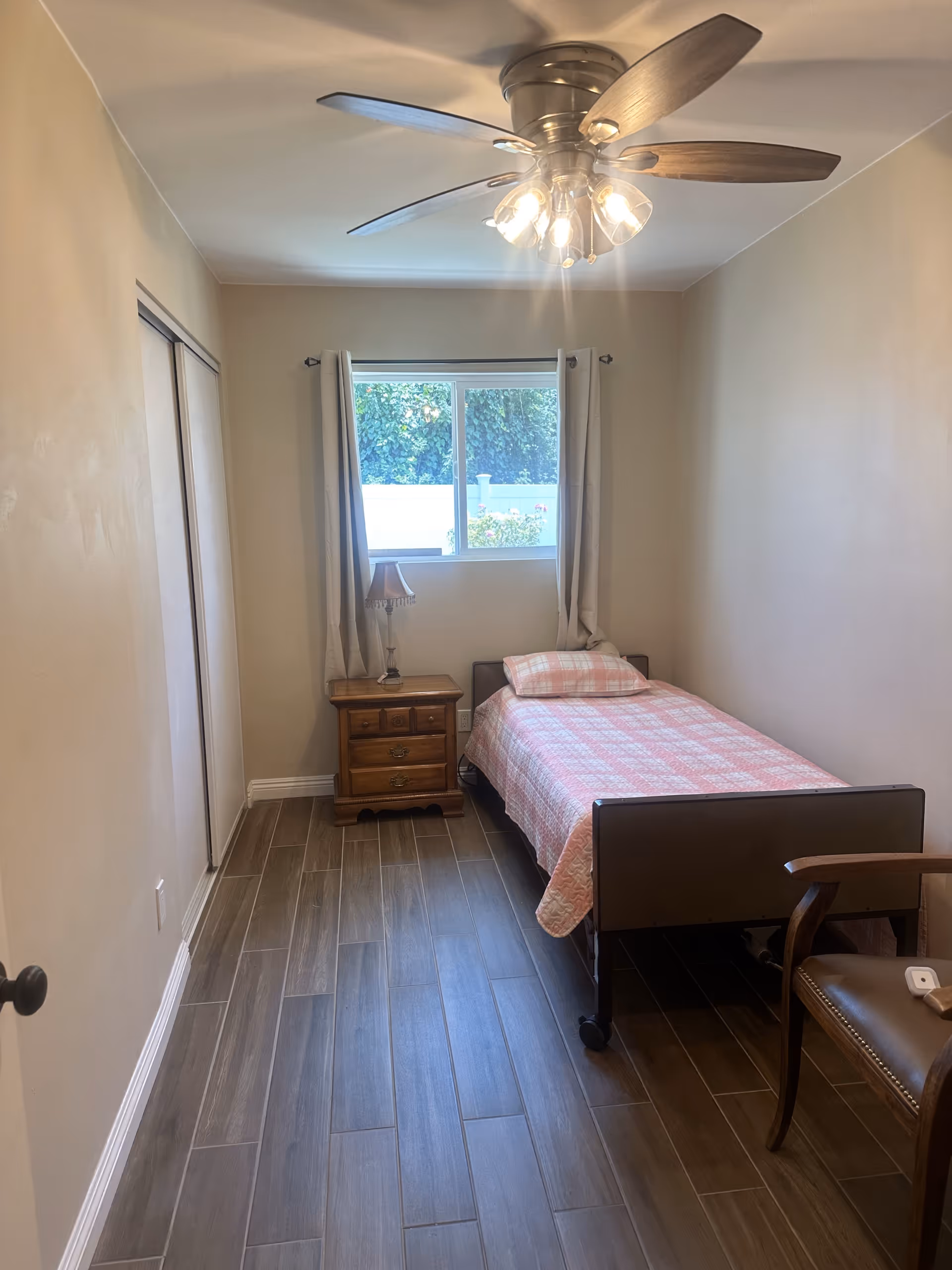 Small bedroom with single bed, nightstand, lamp, window, curtains, and ceiling fan.