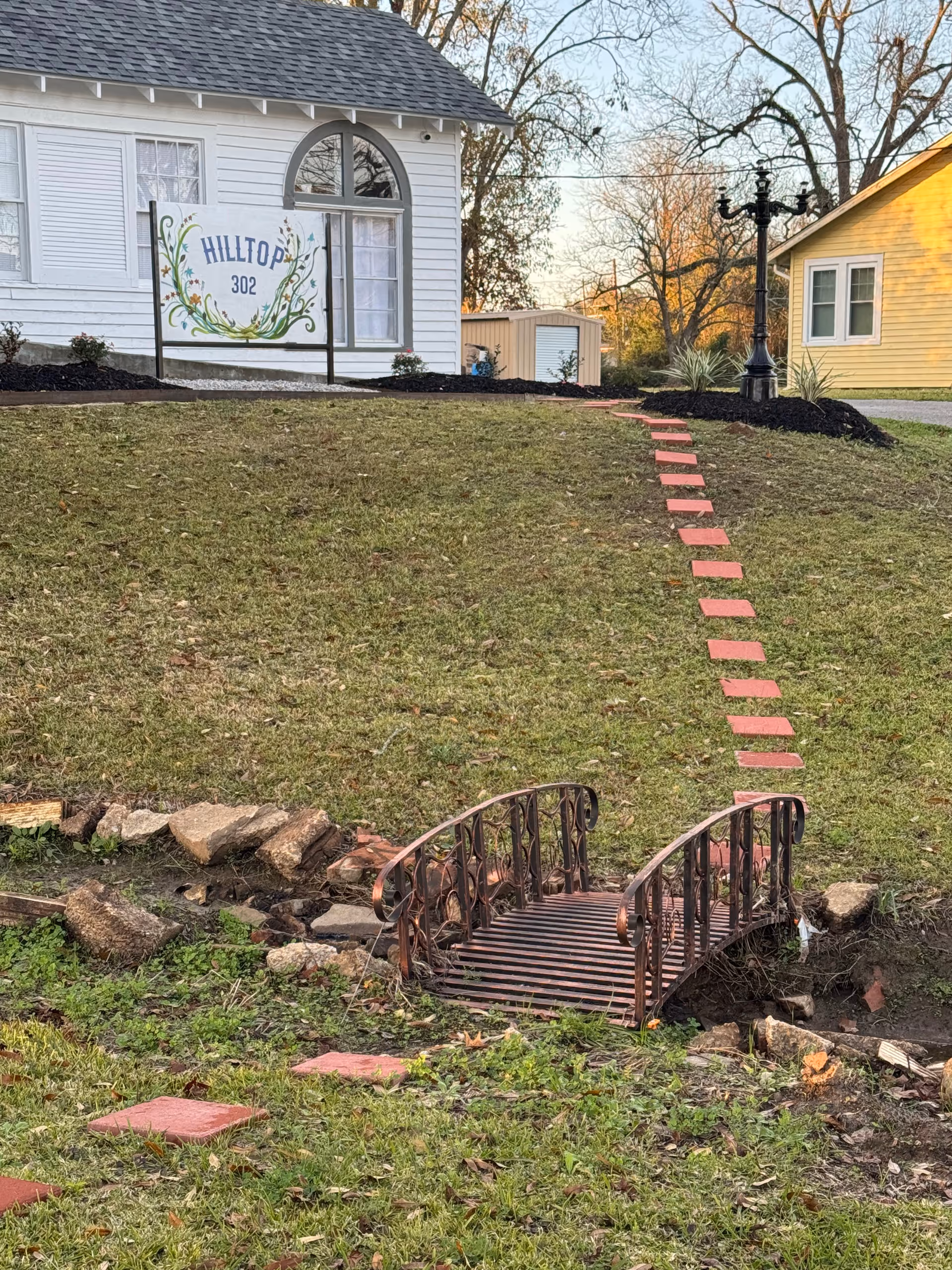 Exterior view of a white Hilltop 302 facility with a grassy hill, bridge, and stepping stones.