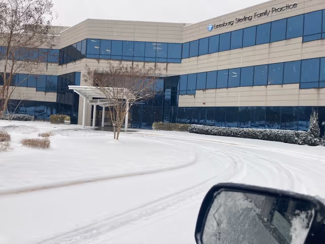 Snow-covered front of a glass-windowed medical building with curved driveway.