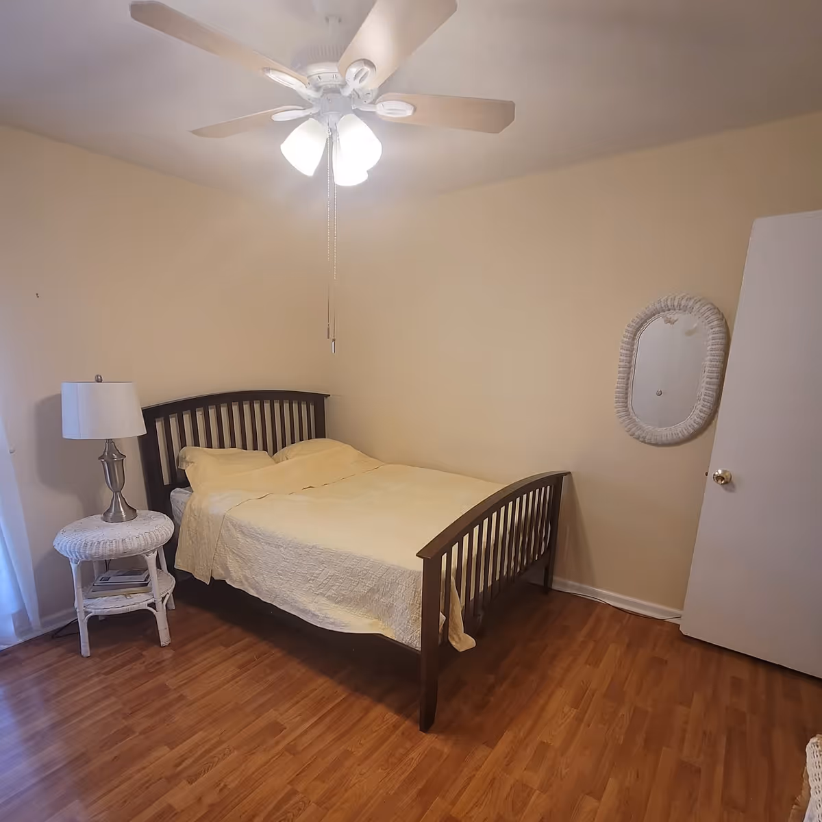 Cozy bedroom with a wooden bed, ceiling fan, nightstand, lamp, and wall mirror.