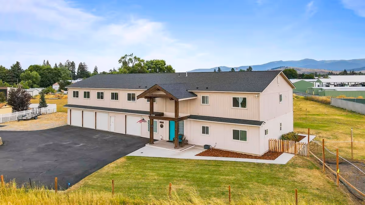 Two-story beige senior living facility exterior with a front porch and multiple garage doors.