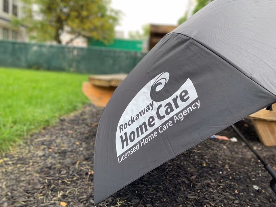Outdoor scene showing a gray umbrella with Rockaway Home Care branding in a yard.