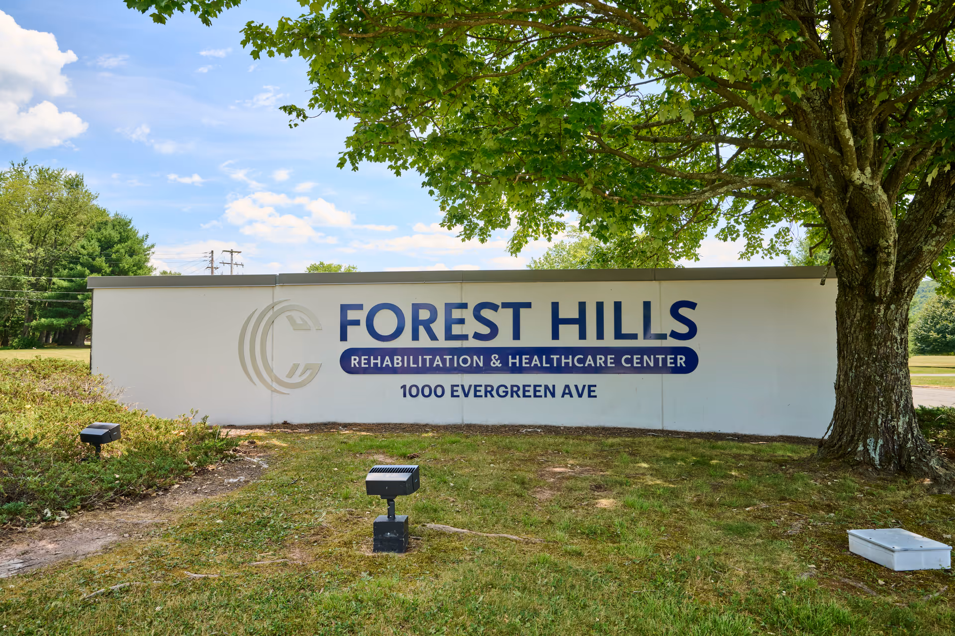 Exterior sign for Forest Hills Rehabilitation & Healthcare Center with lawn and trees.
