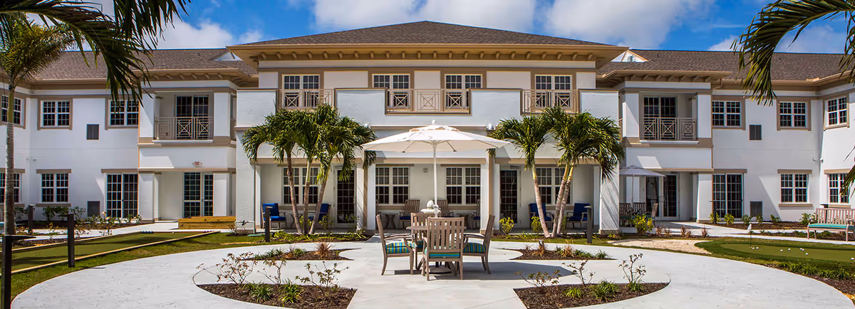 Two-story white building front with a landscaped courtyard, palm trees, patio furniture and a central umbrella.
