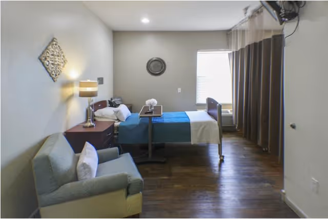 A furnished senior living bedroom with a bed, seating, bedside tables, and curtains.