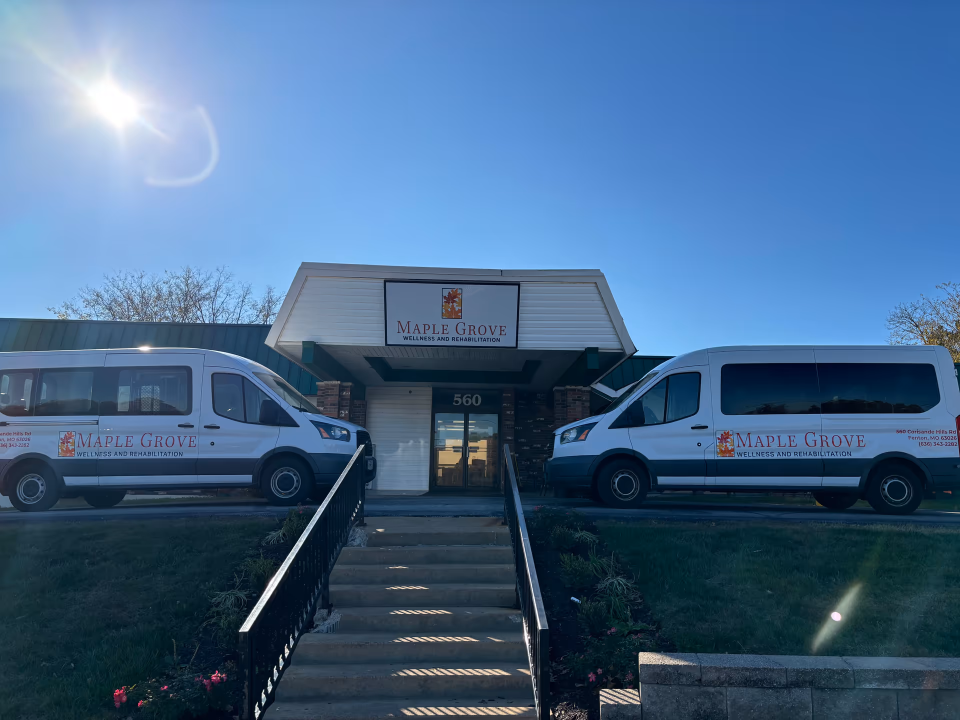 Front view of a building entrance with two white Maple Grove vans parked on either side.