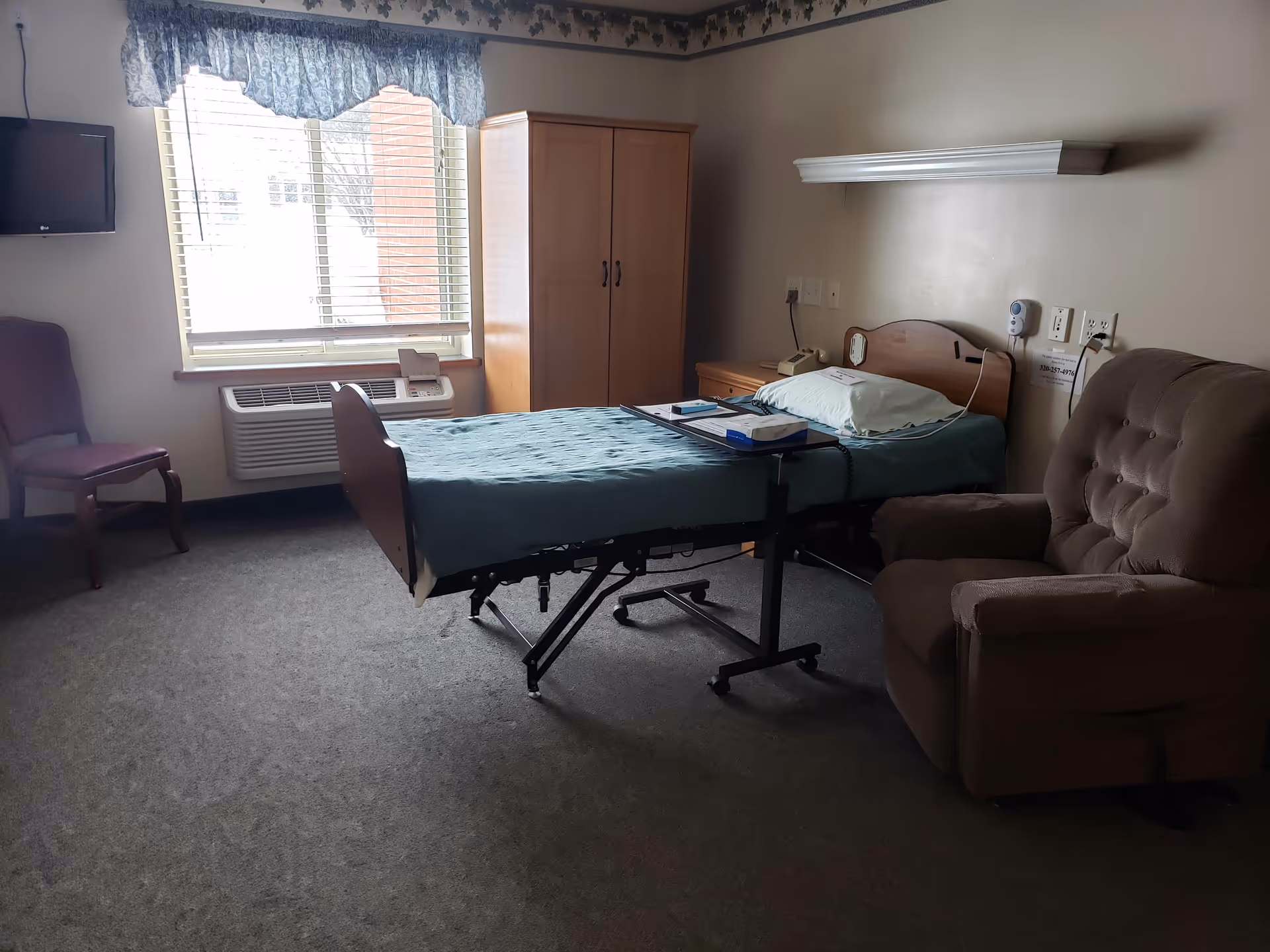 Senior living patient room with a hospital-style adjustable bed, sofa, and window.