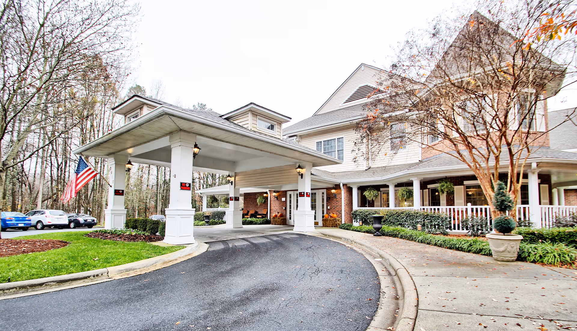 This Charter Senior Living of Charlotte exterior features a covered entrance, drive, and flag.