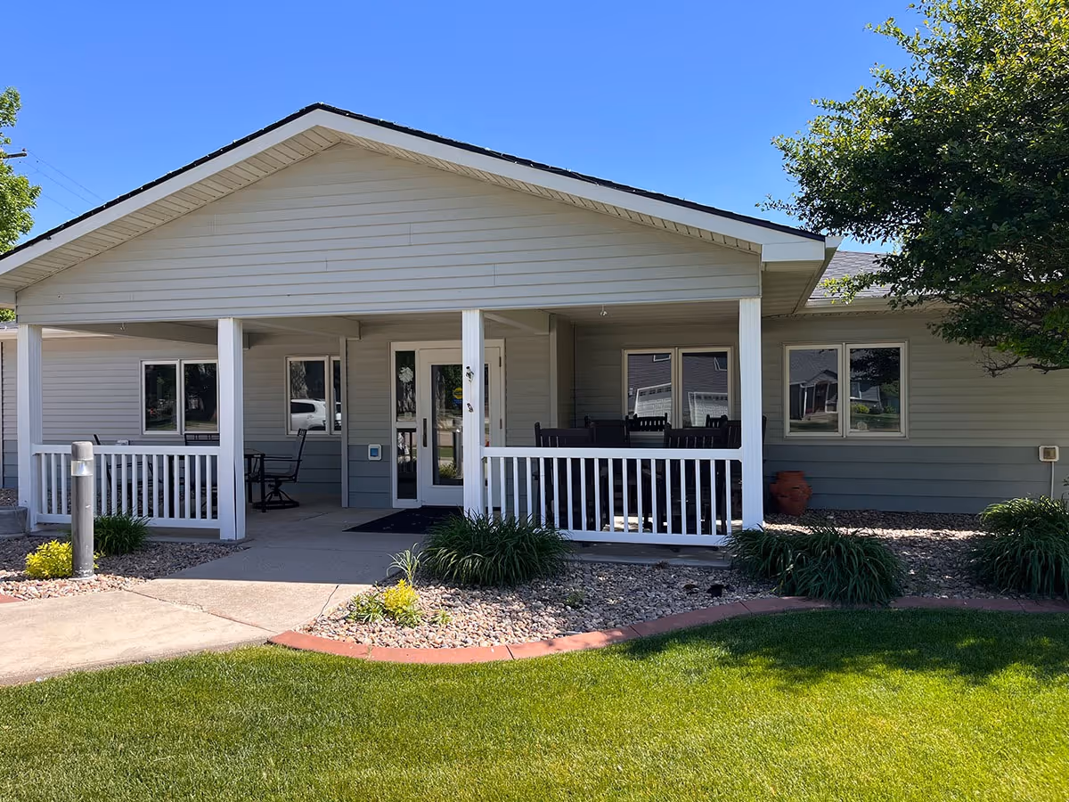 Front exterior of a single-story senior living facility with a covered porch and seating.