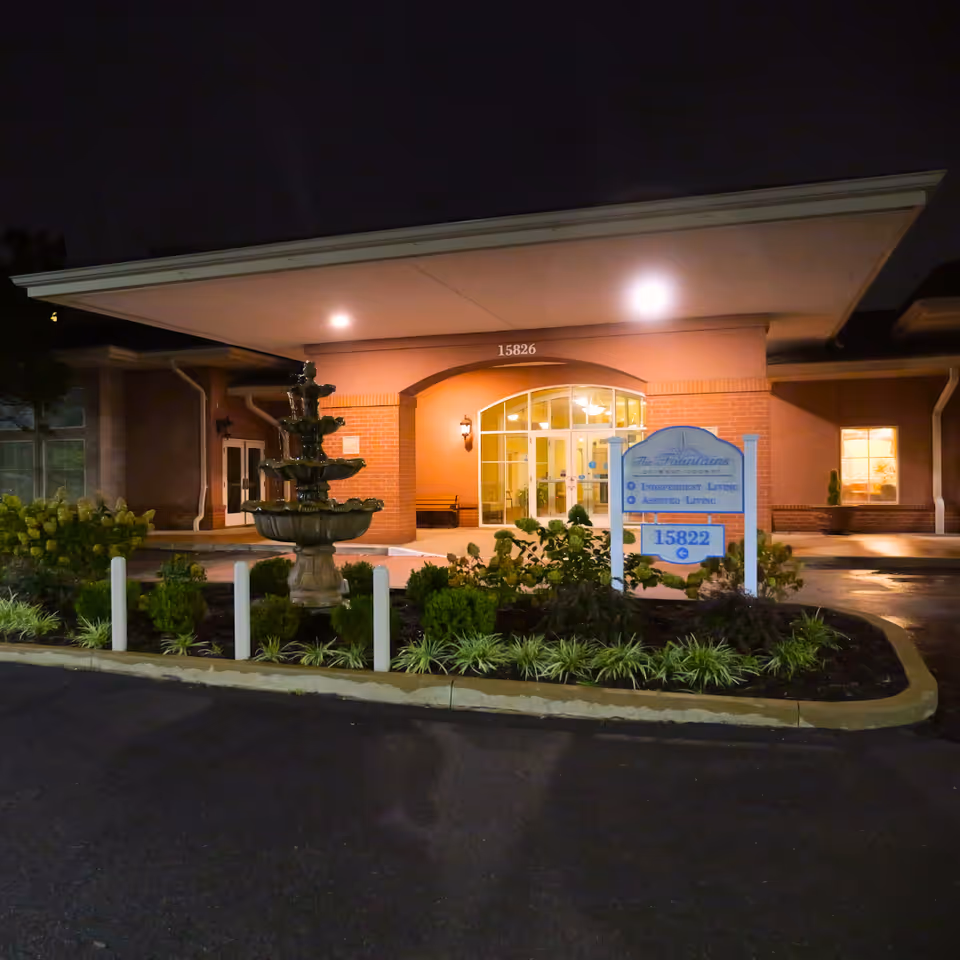 Night view of the front entrance to The Fountains of West County with landscaping