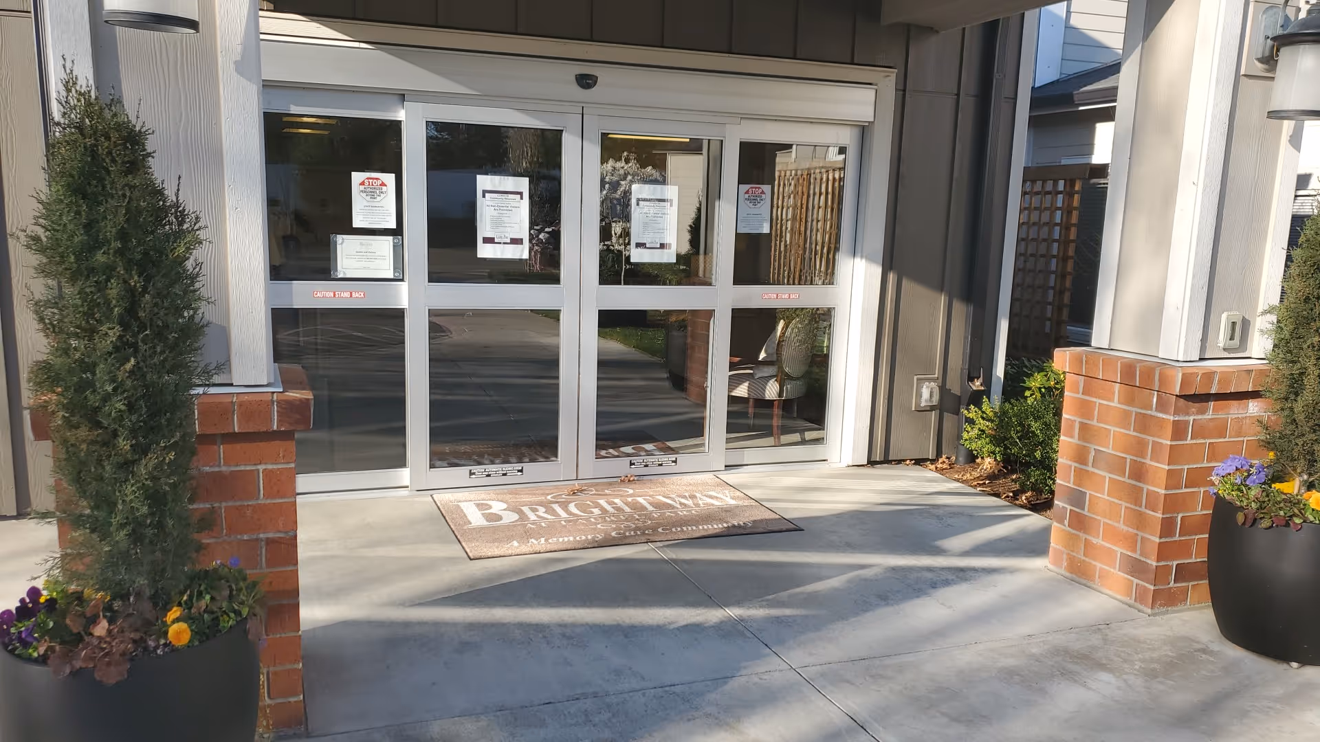 Exterior entrance of a senior living community with glass doors and potted plants.